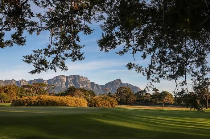 Well-kept golf green beneath a canopy of trees with mountains in the background